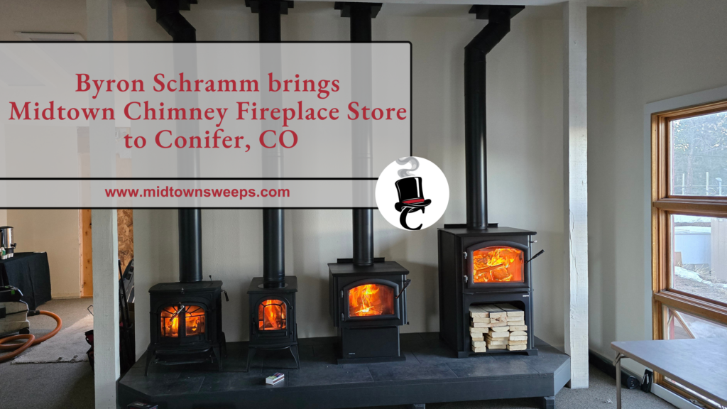 A row of four lit wood-burning stoves and a Fireplace Store display in a showroom, with a sign reading "Byron Schramm brings Midtown Chimney Fireplace Store to Conifer, CO."