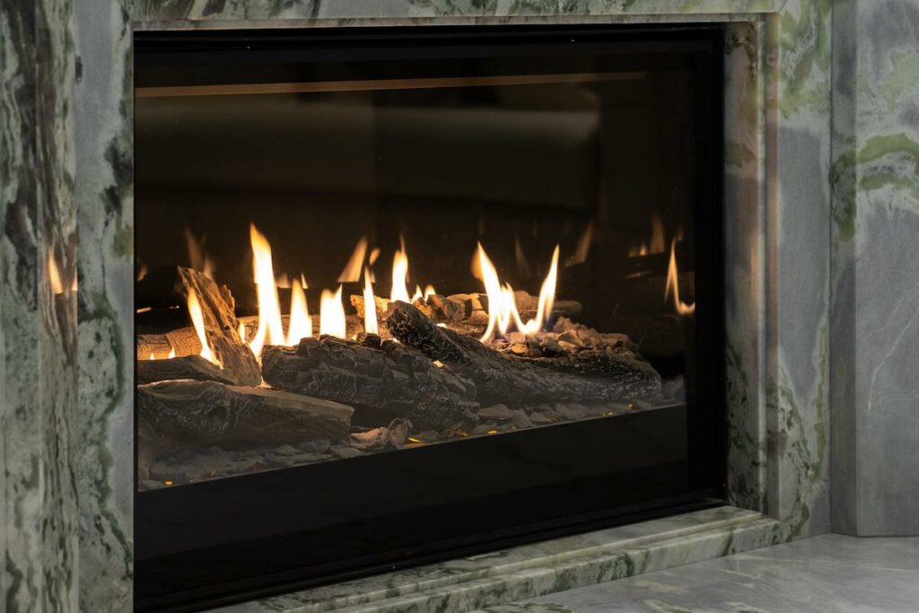 A modern gas fireplace with yellow flames burning among dark logs, set in a gray marble surround.