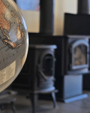 A large globe in the foreground with a black wood stove and fireplace tools in a blurred room behind it.