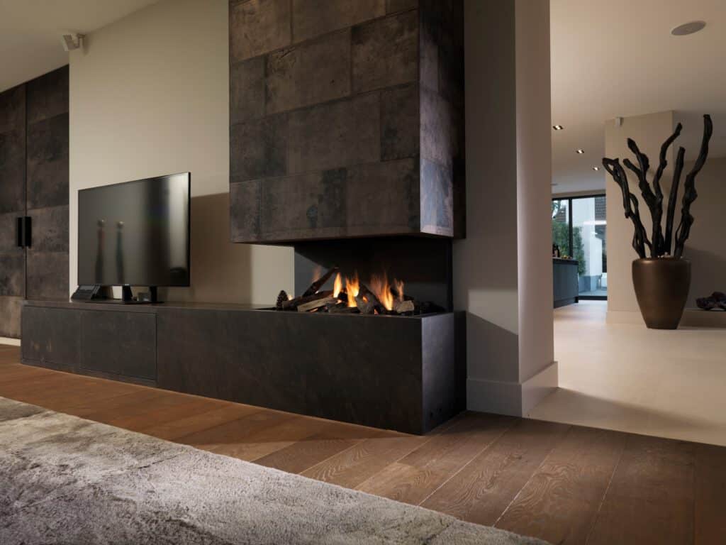 A modern living room with a wall-mounted TV beside a linear fireplace under a dark stone surround, with a hallway and large potted sculpture in the background.