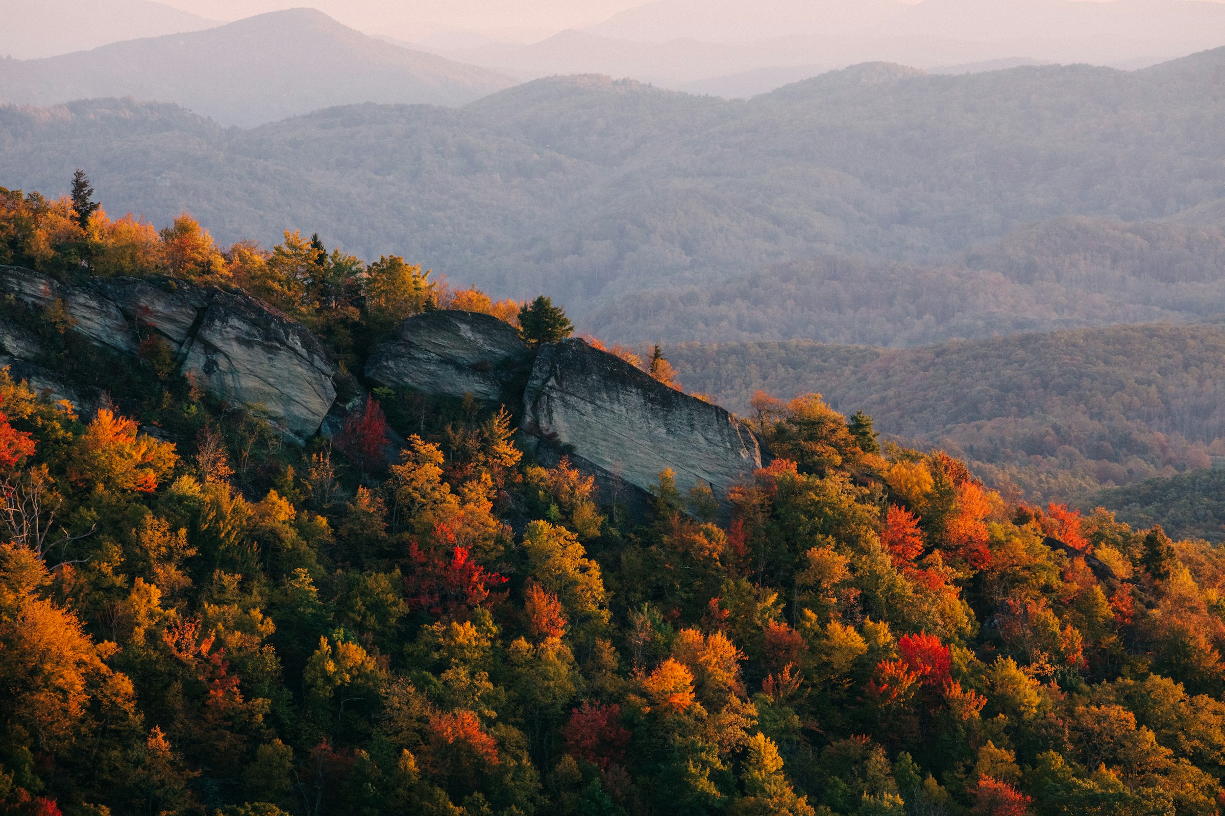 A rocky mountain ridge covered in autumn trees, with layered blue-gray hills fading into the distance.